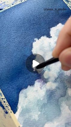 someone is painting clouds with watercolors on paper