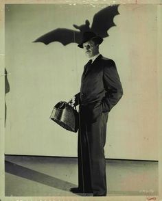 a black and white photo of a man in a suit with a bat on his head