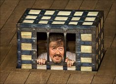 an image of a man looking through the bars of a caged up box that is on top of a wooden floor