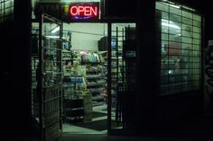 an open sign is lit up in front of a store window at night with the door open