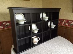 a shelf with cups and saucers on it next to a white bedspread