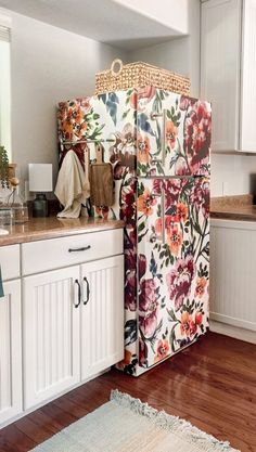 a floral patterned refrigerator in a kitchen with white cabinets and wood floors, along with a rug on the floor