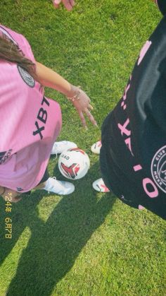 two girls in pink shirts and white shoes with soccer balls on the grass near one another