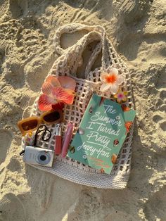 a beach bag with some items on top of it and a camera in the sand