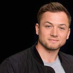 a close up of a person wearing a black jacket and grey t - shirt with a dark background