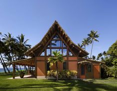 a house with a thatched roof and palm trees on the lawn next to it