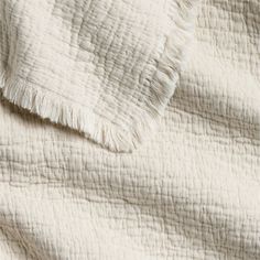 an unmade white quilt with fringes on it