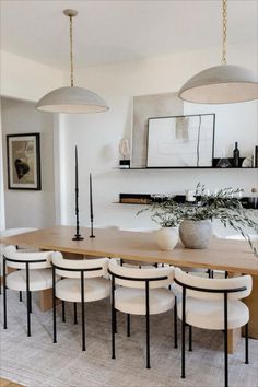 a dining room table surrounded by white chairs and hanging lights over it's head