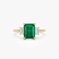 an emerald and diamond ring with three baguets in yellow gold on a white background