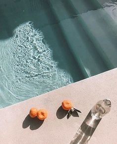 three oranges sitting on the edge of a swimming pool next to a water feature