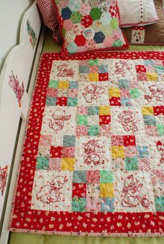 a bed with red and green quilts on it's headboard next to pillows