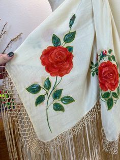 there is a red rose embroidered on a white shawl with tassels around it