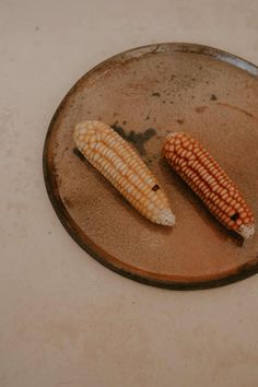 two corn cobs sitting on top of a brown plate next to eachother