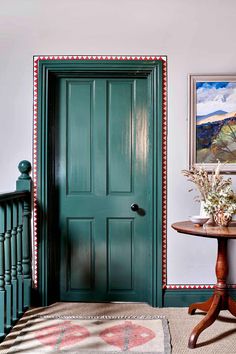 a green door in a white room next to a table with flowers and vases on it