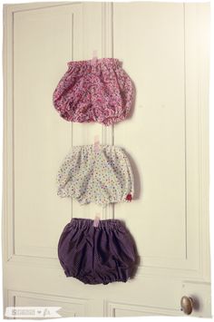 three baby diapers hanging on the wall in front of a white door, one with purple and pink flowers