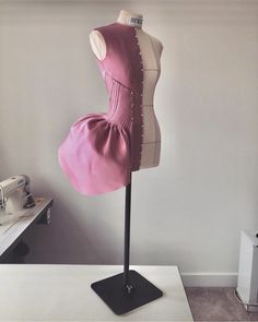 a mannequin with a pink dress on it's stand in front of a white wall