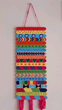 a colorful wall hanging made out of wooden strips and tassels with pink thread