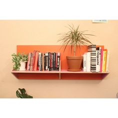 an orange shelf with books and plants on it next to a wall mounted planter