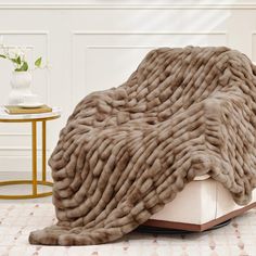 a fur covered chair sitting on top of a white table next to a vase with flowers