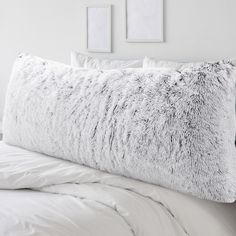 a white bed with two pictures on the wall above it, and a fluffy pillow