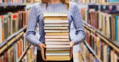 a woman holding a stack of books in a library