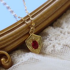 a gold necklace with a red stone in the center on top of a white lace