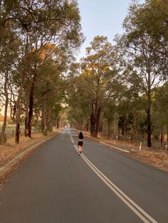 a person walking down the middle of a road with trees on both sides and no cars