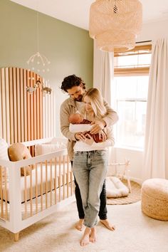 a man and woman standing in a room with a baby next to a crib