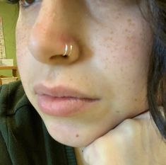 a close up of a person with a nose ring on their left side, wearing a green hoodie