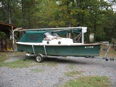 a green and white boat parked in front of a building next to a tree line