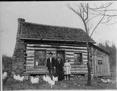 an old black and white photo of three people standing in front of a log cabin