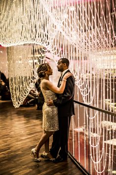 a man and woman standing next to each other in front of a wall covered with lights