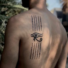 the back of a man with an eye tattoo on his left shoulder and words written in black ink