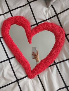 a person taking a photo with their cell phone in front of a heart shaped mirror