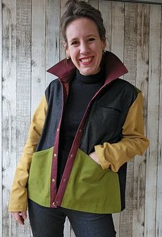 a woman standing in front of a wooden wall wearing a green and yellow jacket with hood