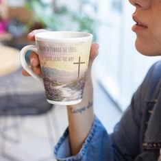 a woman holding a coffee cup with a cross on the side and words above it