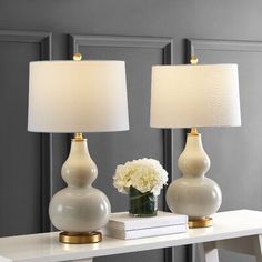 two white lamps sitting on top of a table next to a vase with flowers in it