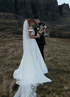 a bride and groom kissing in front of a mountain