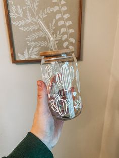 a person holding up a glass jar with some writing on it and a cactus plant in the background