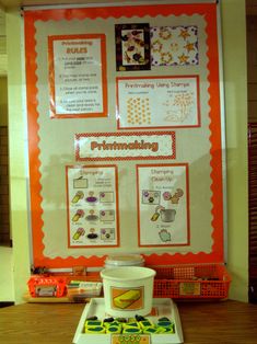 an orange and white bulletin board sitting on top of a wooden table next to a cup