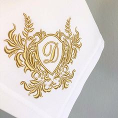 a white napkin with gold embroidered monogrammed initial on the front, and letter d on the back