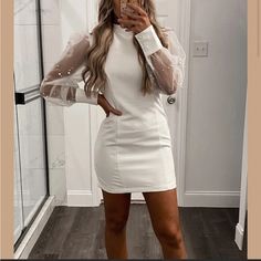 a woman taking a selfie wearing a white dress with sheer sleeves and high heels