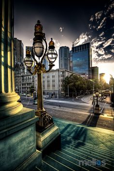 an old fashioned street lamp in the middle of a city with tall buildings behind it