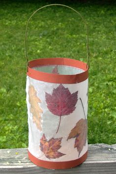 a paper bag with leaves painted on it sitting on a wooden table in front of some grass