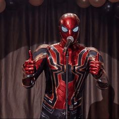 a man dressed as spider - man giving a thumbs up while standing in front of a microphone