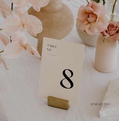 the table numbers are displayed in vases with flowers behind them on a white cloth