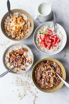 four bowls of oatmeal with strawberries, bananas and granola in them