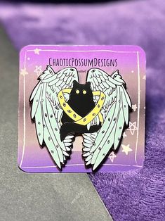 a black cat with angel wings on it's back sitting on a purple blanket