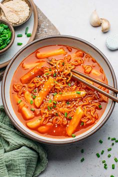 a bowl of noodles and carrots with chopsticks in it next to some vegetables