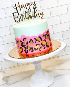 a birthday cake decorated with pink, green and yellow leopard print on a white pedestal